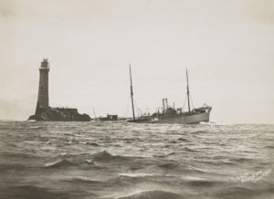 一小块露头上的灯塔旁一艘正在下沉的船的部分视图。